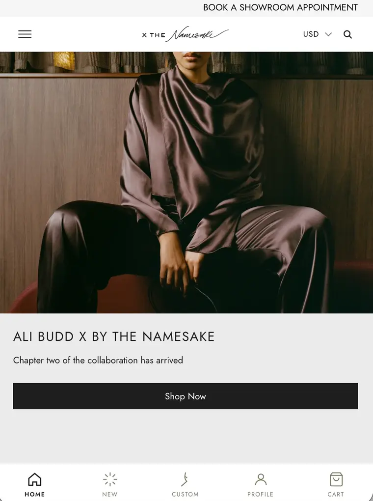 By The Namesake mobile homepage with a collaboration banner image, a Shop Now button and a bottom navigation bar for home, new, custom, profile and cart